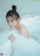 A woman sitting in a bathtub with foam on her face.