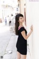 A woman in a black dress leaning against a wall.