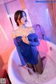 A woman in a blue dress is taking a bath in a bathtub.