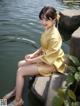 A woman in a yellow kimono sitting on a rock by the water.