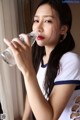 A woman drinking water from a bottle in front of a window.