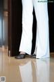 A woman in white pants and black shoes standing in front of a door.