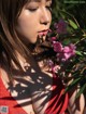 A woman in a red dress smelling a pink flower.